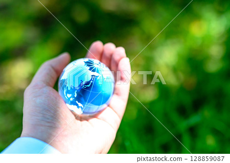 A crystal globe held over beautiful fresh greenery - Ecology image - Blue A crystal globe held over beautiful fresh greenery - Ecology image - Blue 128859087