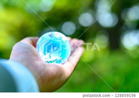 A crystal globe held up against beautiful new greenery - Ecology image - Light blue 128859156