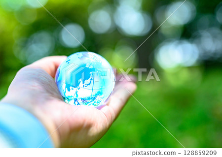 A crystal globe held up against beautiful new greenery. Ecological image. Light blue. 128859209