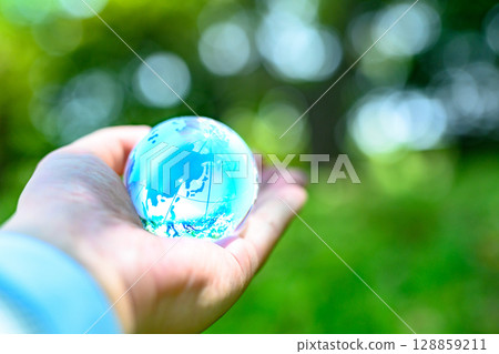 A crystal globe held up against beautiful new greenery - Ecology image - Light blue 128859211