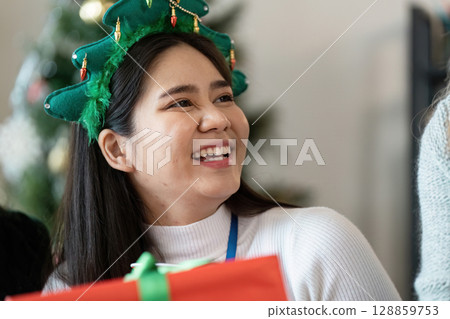 Festive Office Celebration with Smiling Colleague in Christmas Tree Headband and Gift 128859753