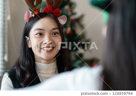 Festive Christmas Office Celebration with Decorated Tree and Happy Employee in Reindeer Antlers Festive Christmas Office Celebration with Decorated Tree and Happy Employee in Reindeer Antlers 128859764