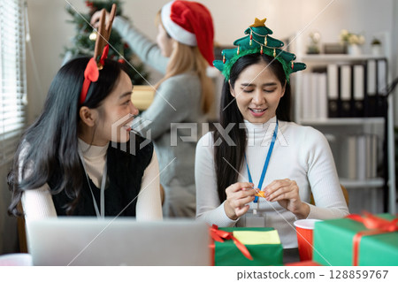 Festive Office Celebration with Colleagues Wearing Christmas Accessories and Decorating a Christmas Tree Festive Office Celebration with Colleagues Wearing Christmas Accessories and Decorating a Christmas Tree 128859767