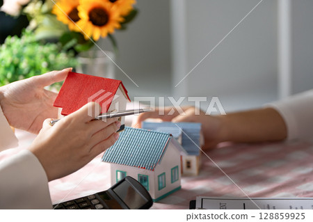 Hands Holding Model Houses with Calculator on Table - Real Estate Investment and Home Buying Concept Hands Holding Model Houses with Calculator on Table - Real Estate Investment and Home Buying Concept 128859925