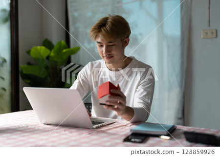 Young Professional Analyzing Real Estate Market Trend on Laptop in Modern Home Office Setting 128859926