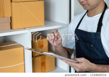 Young Entrepreneur Managing Inventory in a Small Business Warehouse with Cardboard Boxes and Clipboard Young Entrepreneur Managing Inventory in a Small Business Warehouse with Cardboard Boxes and Clipboard 128860016