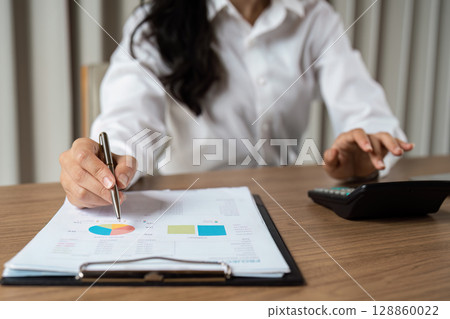 Businesswoman Analyzing Financial Data with Charts and Calculator in Modern Office Setting for Strategic Planning Businesswoman Analyzing Financial Data with Charts and Calculator in Modern Office Setting for Strategic Planning 128860022