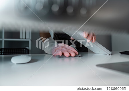 Person Wearing Gloves Cleaning a Modern Office Desk with a Cloth and Keyboard in Focus 128860065