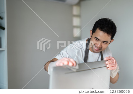 Man Cleaning a Computer Screen with a Cloth in a Modern Home Office Setting 128860066