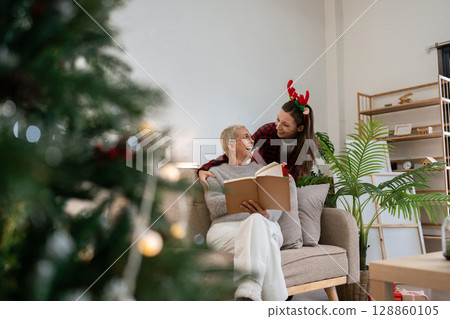 Daughter Surprise gift mother for Christmas while mother was reading book on couch Daughter Surprise gift mother for Christmas while mother was reading book on couch 128860105