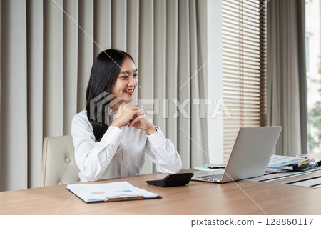 Confident Businesswoman Working on Laptop in Modern Office with Documents and Calculator 128860117