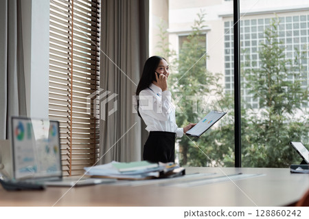 Professional Businesswoman Engaged in a Phone Call in a Modern Office Setting with Natural Light 128860242