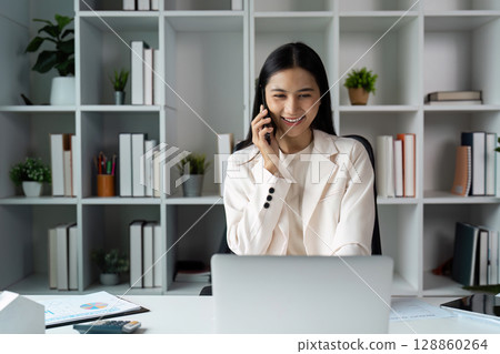 Professional Woman Smiling While Talking on Phone in Modern Office with Laptop 128860264