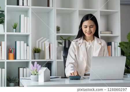 Professional Businesswoman Using Calculator and Laptop for Financial Analysis in Modern Office Setting Professional Businesswoman Using Calculator and Laptop for Financial Analysis in Modern Office Setting 128860297