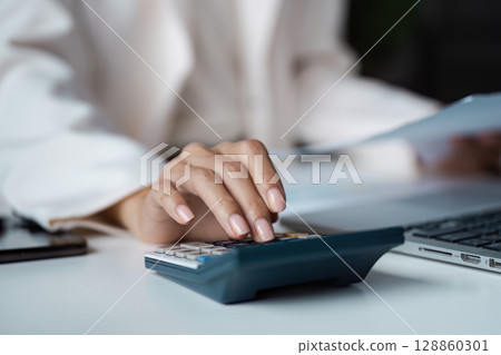 Professional Businesswoman Using Calculator and Laptop for Financial Analysis in Modern Office Setting 128860301