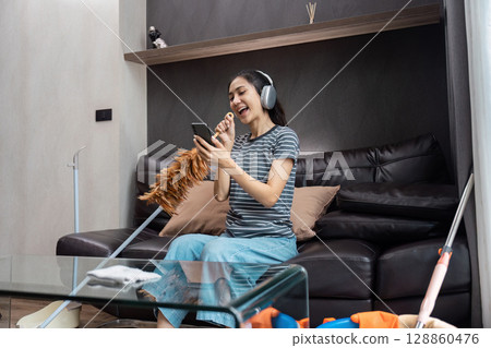 Joyful Housekeeper Singing While Cleaning with Headphones in a Modern Living Room Setting Joyful Housekeeper Singing While Cleaning with Headphones in a Modern Living Room Setting 128860476