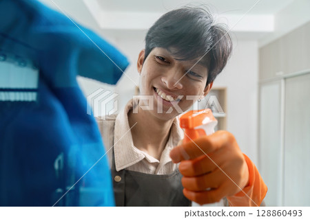 Smiling Housekeeper Cleaning with Spray Bottle and Cloth in Modern Home Interior 128860493