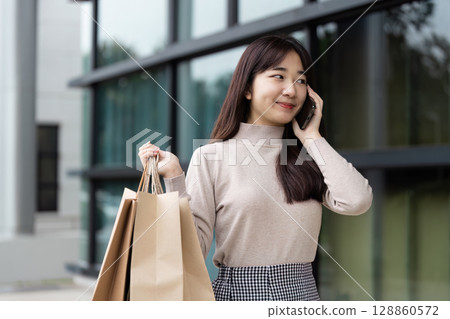 Excited Shopper with Bags on Black Friday Sale Talking on Phone Outside Modern Shopping Mall 128860572