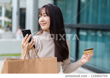 Excited Shopper Holding Smartphone and Credit Card on Black Friday Shopping Spree Outside Modern Retail Store 128860709