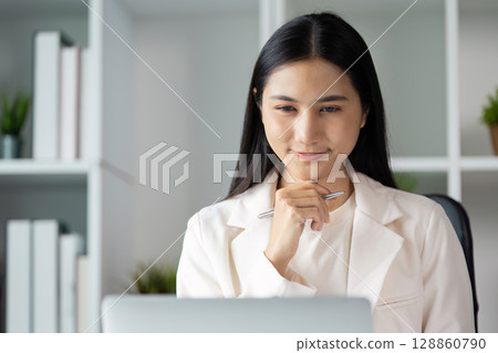 Confident Business Professional Working at Desk in Modern Office with Laptop and Documents, Smiling and Engaged in Productive Work Environment Confident Business Professional Working at Desk in Modern Office with Laptop and Documents, Smiling and Engaged in Productive Work Environment 128860790