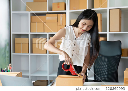 Young Entrepreneur Packing Orders for Online Sales in a Modern Home Office with Shelves of Shipping Boxes Young Entrepreneur Packing Orders for Online Sales in a Modern Home Office with Shelves of Shipping Boxes 128860993
