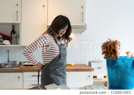 Woman Preparing to Clean Kitchen with Apron in Modern Home, Ready for Housekeeping and Domestic Chores Woman Preparing to Clean Kitchen with Apron in Modern Home, Ready for Housekeeping and Domestic Chores 128861003