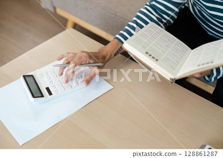 Person Using Calculator and Reading Book at Desk for Financial Planning and Budgeting Person Using Calculator and Reading Book at Desk for Financial Planning and Budgeting 128861287