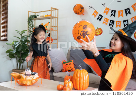 Mother and Daughter Celebrating Halloween at Home with Costumes, Decorations, and Pumpkin-Themed Activities Mother and Daughter Celebrating Halloween at Home with Costumes, Decorations, and Pumpkin-Themed Activities 128861430