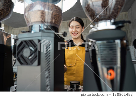 Barista in Yellow Apron Smiling While Preparing Coffee in a Modern Cafe with Professional Equipment Barista in Yellow Apron Smiling While Preparing Coffee in a Modern Cafe with Professional Equipment 128861492