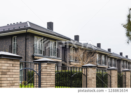 Row of modern brick townhouses with chimneys and fence in upscale suburban development 128861634