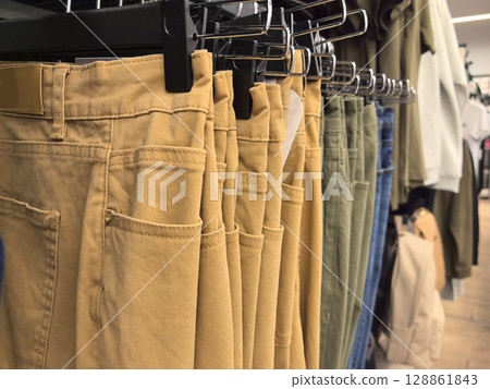 Neutral-toned pants displayed in a chic clothing store during a busy weekend Neutral-toned pants displayed in a chic clothing store during a busy weekend 128861843