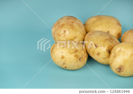Whole fresh potatoes with natural skin placed on a bright turquoise background. Ideal for food and agricultural themes. Whole fresh potatoes with natural skin placed on a bright turquoise background. Ideal for food and agricultural themes. 128861946
