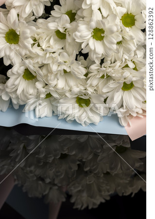 flowers chrysanthemum with white petals closeup, fresh white chrysanthemum flowers in a large gift bouquet, flowers are reflected on black glass flowers chrysanthemum with white petals closeup, fresh white chrysanthemum flowers in a large gift bouquet, flowers are reflected on black glass 128862392
