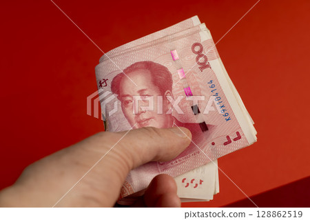 holding a large stack of Chinese yuan in his hand on a red background, holding a large amount of money in yuan in the hands of a man 128862519
