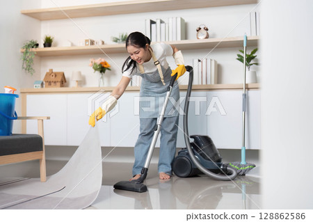 Home Cleaning. Young woman vacuuming the floor with focus and care. 128862586