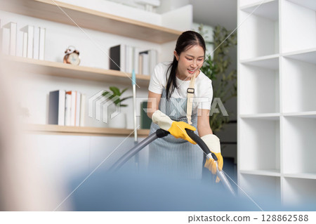 Home Cleaning. Joyful woman vacuuming while listening to music in a modern living room. Home Cleaning. Joyful woman vacuuming while listening to music in a modern living room. 128862588