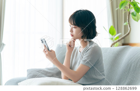A woman thinking while looking at her smartphone A woman thinking while looking at her smartphone 128862699