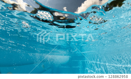 Underwater view of a backyard pool with steps, bubbles, and shimmering reflections, showing the surface tension and sky clouds from below the water. Underwater view of a backyard pool with steps, bubbles, and shimmering reflections, showing the surface tension and sky clouds from below the water. 128862958