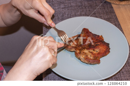 Woman cut of pieces of steak on ceramic plate 128864210