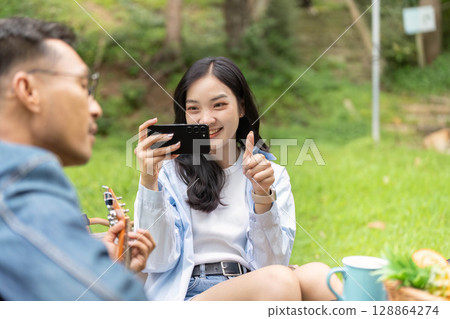 Outdoor Fun. Young woman capturing joyful moment with smartphone in nature. 128864274
