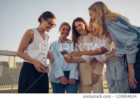 Friends are enjoying their smartphones together in a beautiful outdoor setting, filled with joy Friends are enjoying their smartphones together in a beautiful outdoor setting, filled with joy 128864624