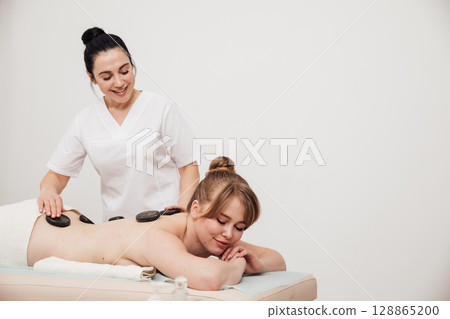 Massage therapist doing medical back massage with stones to woman Massage therapist doing medical back massage with stones to woman 128865200