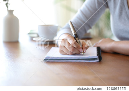 Woman hand writing with a pen on notebook on a table 128865355