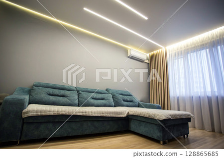 Interior in the hall: blue large sofa against the background of a window with brown curtains and wooden laminate. Modern interior room hall. Copy space for text Interior in the hall: blue large sofa against the background of a window with brown curtains and wooden laminate. Modern interior room hall. Copy space for text 128865685