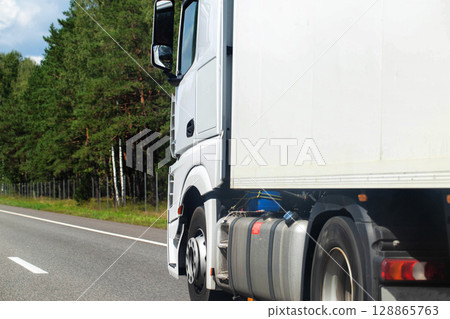 A white new truck is carrying cargo to an online store against the backdrop of a forest. Copy space for text A white new truck is carrying cargo to an online store against the backdrop of a forest. Copy space for text 128865763