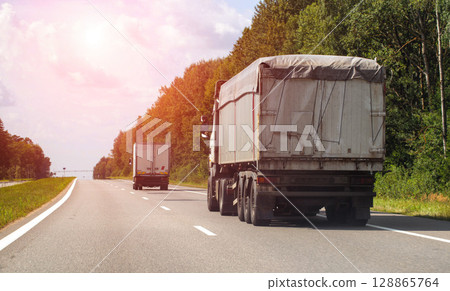 A truck with a semi-trailer for bulk agricultural cargo transports grain along a highway in summer, copy space for text, industry 128865764