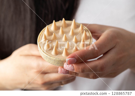 Girl holding head massager against black hair background. Improving blood circulation, head massage, close-up. Hair care Girl holding head massager against black hair background. Improving blood circulation, head massage, close-up. Hair care 128865787