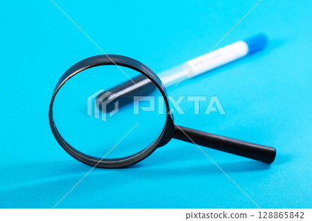 A magnifying glass against the background of a sterile test tube with an analysis for vitamins and a blue background. Analysis for a complex of vitamins, micro and macroelements, close-up 128865842