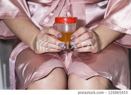 The girl holds a urine test in her hands. Concept of sand in urine, cystitis and pyelonephritis. Urinary tract infections, close-up The girl holds a urine test in her hands. Concept of sand in urine, cystitis and pyelonephritis. Urinary tract infections, close-up 128865855