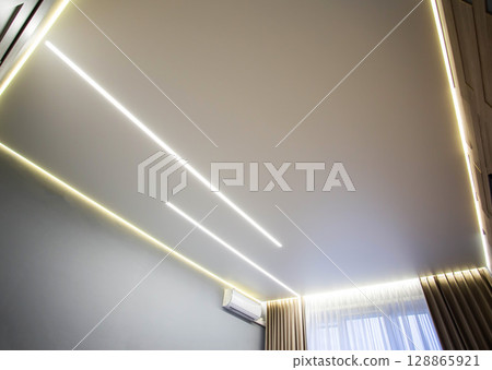 Beautiful modern stretch ceiling with yellow LED lines around the perimeter. Designer stylish ceiling in the hall. 128865921